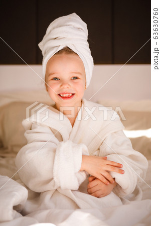 Little girl in a bathrobe and with a turban on her head in a white bed. 63630760