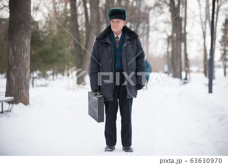 An old man with case standing outdoors in winter park An old man with case standing outdoors in winter park 63630970