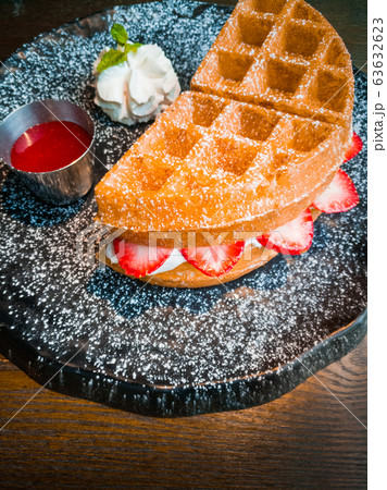 Strawberry waffles and whipped cream, garnished with mint leaves, served with strawberry sauce on a black plate, sprinkled with icing 63632623