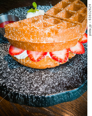 Strawberry waffles and whipped cream, garnished with mint leaves, served with strawberry sauce on a black plate, sprinkled with icing Strawberry waffles and whipped cream, garnished with mint leaves, served with strawberry sauce on a black plate, sprinkled with icing 63632624