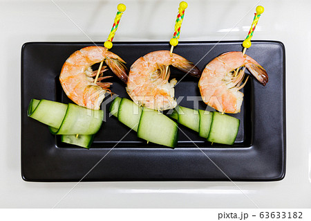 Canapes with tiger prawn on cucumber on black plate 63633182