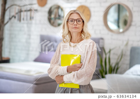 Serious business woman clutching a yellow notebook for notes. 63634134