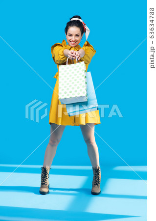 Young woman in a mustard dress standing with bags in her hands Young woman in a mustard dress standing with bags in her hands 63634788