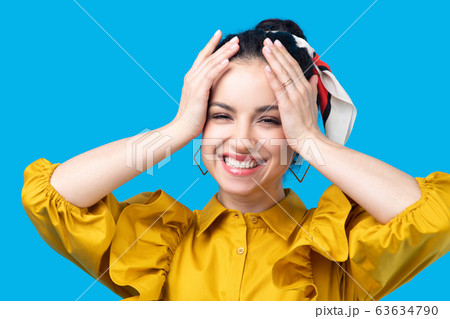 Young woman in a mustard dress holding her head and smiling Young woman in a mustard dress holding her head and smiling 63634790
