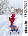 Winter fun. Beautiful little girl in a red coat and mittens smiles and holds a sled on a rope. Snow covered path, trees and snowdrifts. Frosty snowy weather. Clear winter day. Pleasure at fresh air 63637592