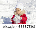Winter activities for children. A little girl is trying to make a snowball. She is dressed in a bright red coat with a white hat and scarf and mittens. Wonderful pastime in the winter. Portrait 63637598