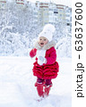 Enjoyment in the winter season. A beautiful little girl in a red coat and white hat with a scarf runs along a snowy path in a winter park. Smile and children's joy on the face. Great holidays. Snow 63637600