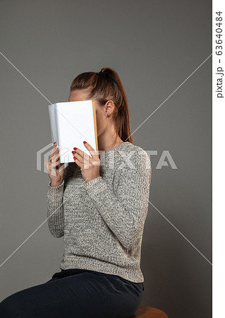 Happy world book day, read to become someone else - woman covering face with book while reading on grey background Happy world book day, read to become someone else - woman covering face with book while reading on grey background 63640484