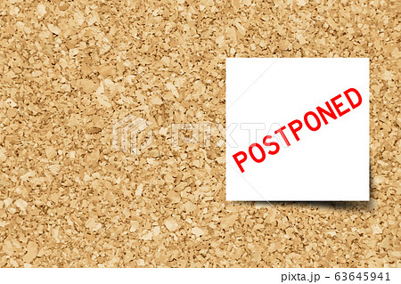 White note with word postponed on cork board background 63645941