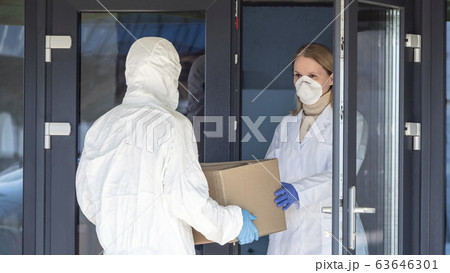 A person in a protective suit is handed a box of medicines to a doctor at the entrance to the hospital A person in a protective suit is handed a box of medicines to a doctor at the entrance to the hospital 63646301