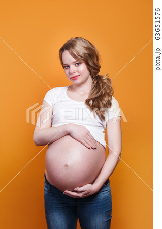 Pregnant happy woman touching her belly on yellow background Pregnant happy woman touching her belly on yellow background 63651576