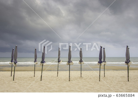Many umbrellas on the sandy beach Background sea and black rain clouds. 63665884