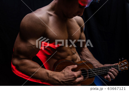 Muscular man with naked torso with ukulele and smoked colorful background  63667121