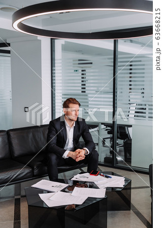 Handsome stylish confident businessman in a smart suit sitting on a sofa in the office. 63668215