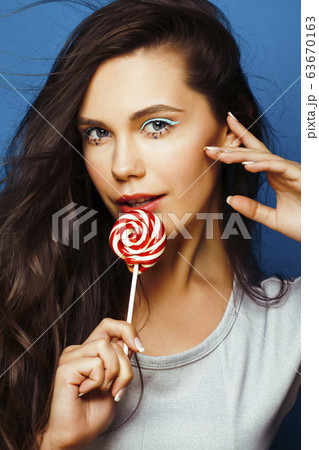 young pretty adorable brunette woman with candy close up posing on blue background, like doll makeup, fashion beauty people concept 63670163