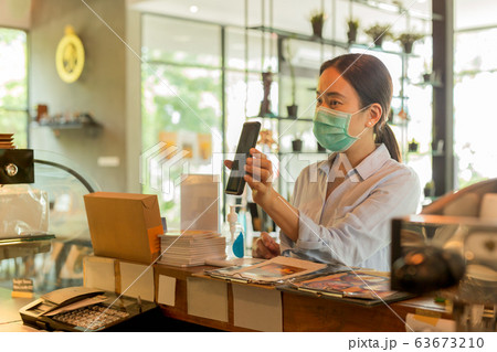 Woman customer with protective mask paying bill by cell phone in cafe. 63673210