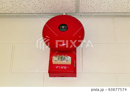 A red fire alarm hanging on a white brick wall A red fire alarm hanging on a white brick wall 63677574