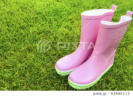 Pink rubber boots stand on green grass. 63680113
