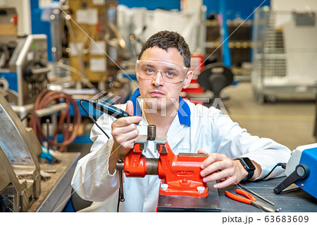 worker in metal processing plant grinds metal component on vise 63683609