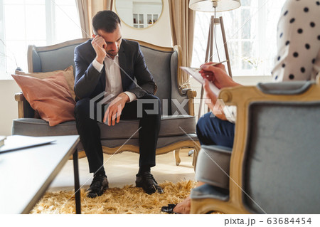Low-spirited dark-haired man sitting on a sofa Low-spirited dark-haired man sitting on a sofa 63684454