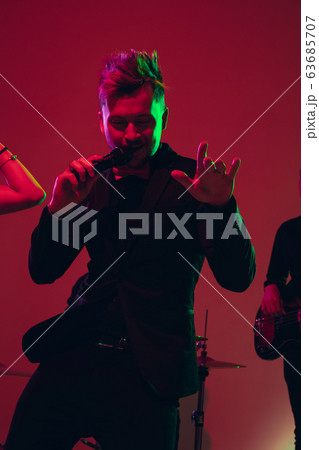 Young caucasian musician, singer performing in neon light on red studio background Young caucasian musician, singer performing in neon light on red studio background 63685707