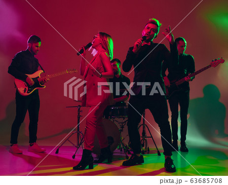 Young caucasian musicians, band performing in neon light on red studio background Young caucasian musicians, band performing in neon light on red studio background 63685708