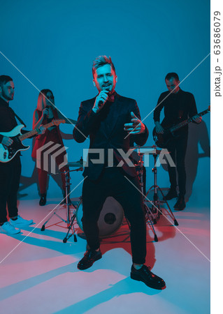 Young caucasian musicians, band performing in neon light on blue studio background, singer in front 63686079