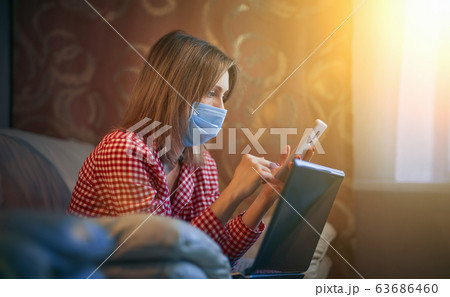 Young european woman wearing surgical face mask stay at home during coronavirus, covid-19 outbreak and looking news or application on smartphone 63686460
