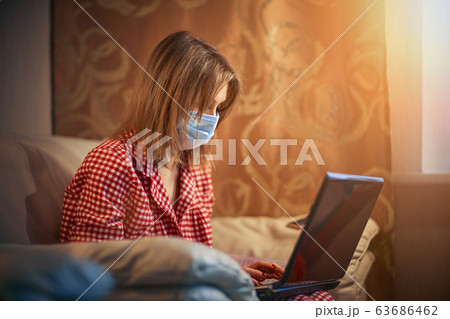 Young businesswoman in a medical protective mask works from home at the computer during self-isolation and quarantine. Virus coronavirus outbreak, flu epidemic and covid ncov novel. Stay home 63686462