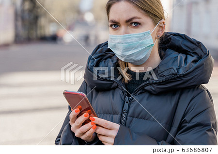 Pportrait of woman in protective medical mask using smart phone on empty european streets. Health and safety, N1H1 coronavirus, covid-19, virus protection care and medical concept. Pan left shot. 63686807