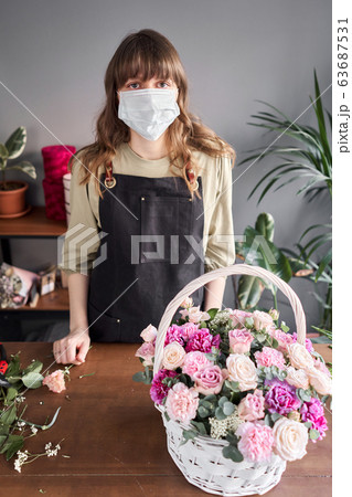 Florist woman in a medical mask for protection from coronavirus. Pandemic concept, working during an epidemic. Small flower shop. Flowers delivery. Florist woman in a medical mask for protection from coronavirus. Pandemic concept, working during an epidemic. Small flower shop. Flowers delivery. 63687531