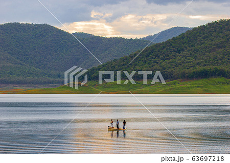 Three men standing on the boat and fishing in middle of the dam among mountain. 63697218