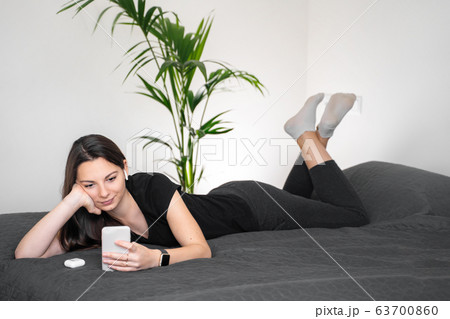 Young woman using phone and wireless earphones on the bed. Stay home during quarantine Young woman using phone and wireless earphones on the bed. Stay home during quarantine 63700860