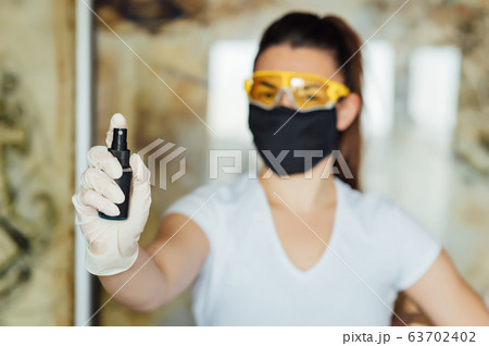 A girl in a protective mask, glasses and gloves spray an antiseptic to prevent infection. A girl in a protective mask, glasses and gloves spray an antiseptic to prevent infection. 63702402