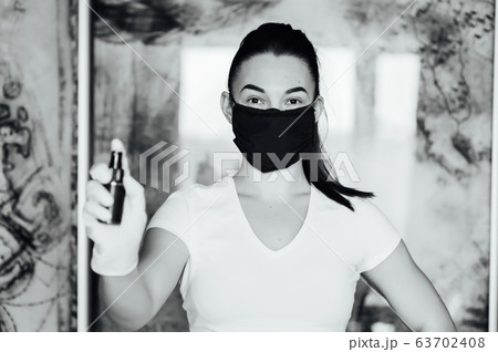 A girl in a protective mask, glasses and gloves spray an antiseptic to prevent infection. A girl in a protective mask, glasses and gloves spray an antiseptic to prevent infection. 63702408