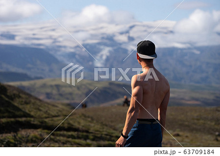 Backside of tall muscular caucasian man with naked torso standing in over mountain and sky background. Promoting active, sport and healthy lifestyle Backside of tall muscular caucasian man with naked torso standing in over mountain and sky background. Promoting active, sport and healthy lifestyle 63709184