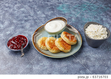 Cottage cheese pancakes with raspberry jam.Russian syrniki or sirniki, cottage cheese fritters or pancakes with a bowl of fresh homemade cottage cheese on dark grey background 63716703