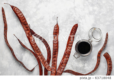 Carob syrup in glass jar with carob pods and seeds on light background Carob syrup in glass jar with carob pods and seeds on light background 63718048