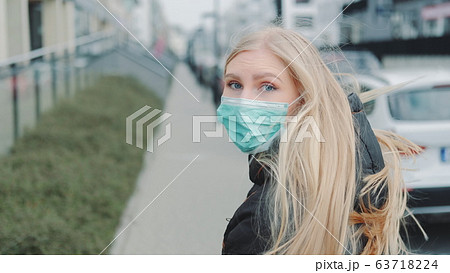 Young blonde woman in a medical mask escaping from somebody on the street. Young blonde woman in a medical mask escaping from somebody on the street. 63718224