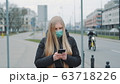 Coronavirus pandemic: blonde woman in a medical mask writing message on smartphone 63718226