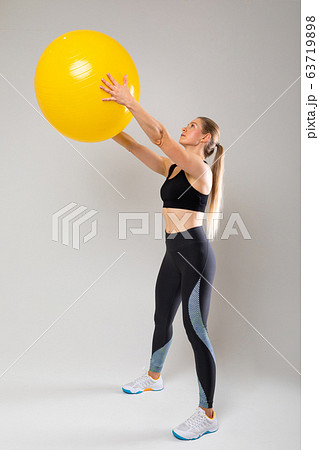 slim fit blonde girl in a sports uniform is engaged in physical exercises on a gray background slim fit blonde girl in a sports uniform is engaged in physical exercises on a gray background 63719898