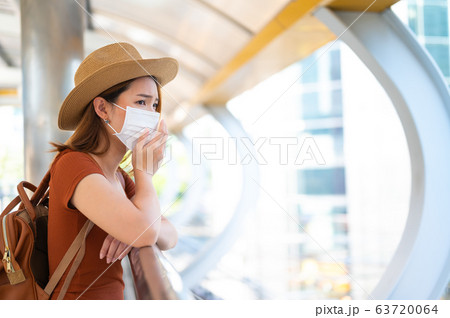 Young woman wearing surgical mask coughing while standing public 63720064
