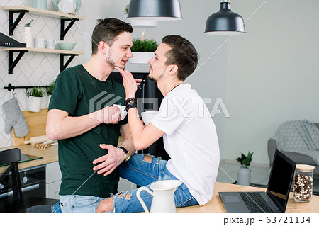 Young homosexual lovers looking at one another at home. Happy smiling gay couple drinking coffee together at kitchen 63721134