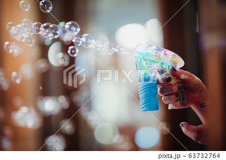 A man's hand uses a bubble gun to blow bubbles 63732764