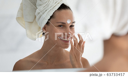 Woman applies day facial moisturizer cream on face closeup Woman applies day facial moisturizer cream on face closeup 63733457