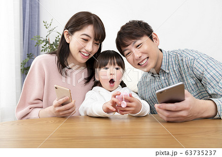 スマートフォンを持つ両親とキッズケータイを持つ女の子　家族イメージ 63735237