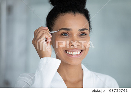 African beautiful woman tweezing eyebrows with tweezers 63736741