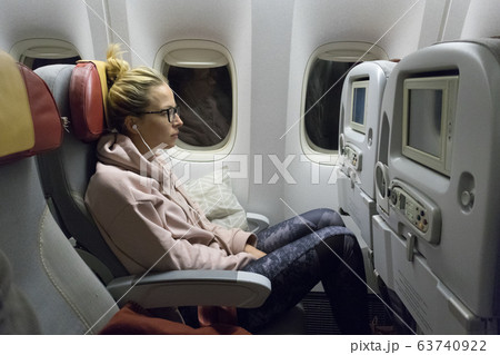 Sporty casual young blonde caucasian lady watching movie while traveling by airplane by the window. Commercial transportation by planes Sporty casual young blonde caucasian lady watching movie while traveling by airplane by the window. Commercial transportation by planes 63740922
