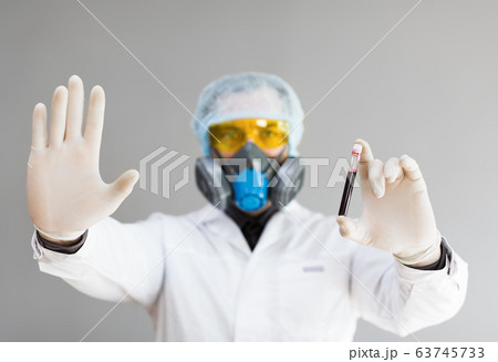 Photo of a doctor in protective clothing holds a test tube with a sample of infected blood in his hand and showing stop sign by another hand. Photo of a doctor in protective clothing holds a test tube with a sample of infected blood in his hand and showing stop sign by another hand. 63745733