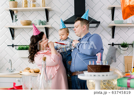 Happy Family, father, mother and little baby boy blowing in party horns on birthday party at home. Portrait of a parents celebrating little their son's first birthday Happy Family, father, mother and little baby boy blowing in party horns on birthday party at home. Portrait of a parents celebrating little their son's first birthday 63745819